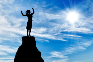 Silhouette of a business woman at the peak of the mountain on the background of the sunny sky